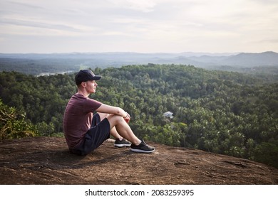 Pensive man resting at the edge of a rock and looking at view. Landscape with tropical rainforest in Sri Lanka.