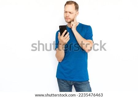 Pensive man thinking and holding mobile phone. Focused bearded man standing on white background, thinking about worried news or what to reply on message. Online communication, cyberspace concept