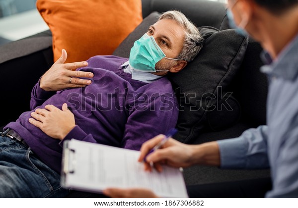 Pensive\
man wearing a face mask while lying down on psychiatrist\'s couch\
and talking about his issues with a therapist,\
