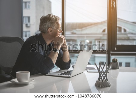 Pensive mature businessman having job with laptop while looking at window. Contemplative employer concept