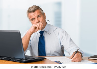 Pensive mature businessman looking up with concentration and writing in his paperwork at office - Powered by Shutterstock