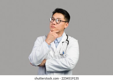 Pensive mature chinese guy therapist in white coat and glasses thinks and looks at free space, isolated on gray background, studio. Doctor choice, idea and solution for treatment, medical health care - Powered by Shutterstock