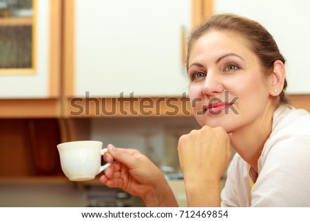 Pensive mature woman holding cup of coffee in kitchen. Housewife female with hot energizing beverage. Caffeine energy.