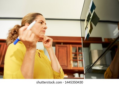 Pensive Mature Woman Making Grocery List And Sticking Notes On Fridge Before Going To Supermarket