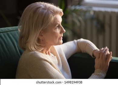 Pensive Mature Woman Sit On Couch Look In Distance Thinking Of Past Happy Days Remembering Young Years, Thoughtful Senior Wife Widow Mourning After Late Deceased Husband, Grieving At Home