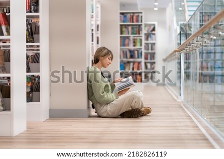 Pensive middle-aged Scandinavian woman book lover spending free leisure time in library, mature female with book in hands sitting in lotus pose on floor near bookcase, enjoying reading. Hobby concept Сток-фото © 