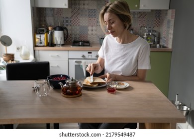 Pensive Middle-aged Single Woman In Home Wear Sit Alone At Table In Kitchen, Enjoying Breakfast In Peace And Quiet At Home, Mature Lone Lady Eating Healthy Food In Morning, Spreading Butter On Toast