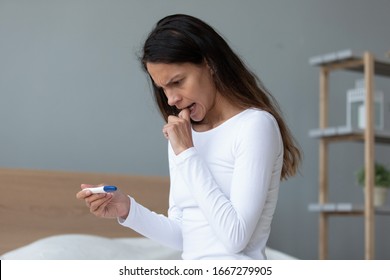 Pensive Millennial Girl Sit In Bed At Home Hold Test Thinking Of Possible Pregnancy, Anxious Thoughtful Young Woman Look At Test Results Feel Worried About Infertility, Female Health Problem Concept