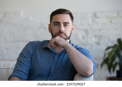 Pensive Millennial Man Sit On Couch In Living Room Staring At Camera. Profile Picture Of Handsome Single Guy Spend Leisure Alone Relaxing At Home. Tenancy, Young Homeowner Or Renter Portrait Concept