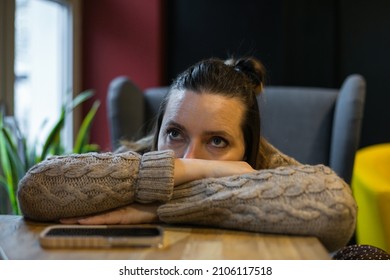 Pensive millennial woman having bad day lying with head on hand on table near window at cafe, lost in unpleasant thoughts. Melancholy, disappointment, indifference - Shutterstock ID 2106117518