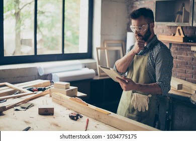 Pensive minded concentrated confident handsome bearded wearing checkered shirt cabinet-maker is watching online videos on the internet how to process wood, he is holding digital tablet - Powered by Shutterstock