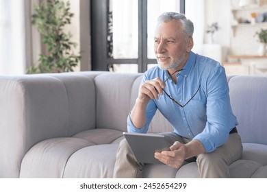 Pensive old elderly senior man with grey hair, grandfather using digital tablet for online work, e-learning, social media, reading electronic book at home. social distance and lockdown concept - Powered by Shutterstock