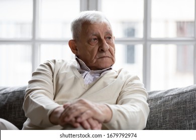 Pensive Old Man Resting At Home Sitting On Couch In Living Room Alone. Aged 80s Baby Boomer Older Generation Male Lost In Sad Thoughts Feels Lonely, Recollect Life Moments Has Nostalgic Mood Concept