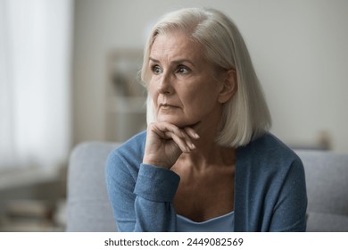 Pensive old woman sits at home alone, look aside, deep in thoughts about health problems, feel anxious, suffer from sadness, try to find answers to issues. Melancholy, loneliness, life on retirement - Powered by Shutterstock