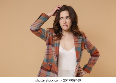 Pensive preoccupied confused young brunette woman 20s in casual checkered jacket posing standing put hand on head biting lips looking aside isolated on pastel beige colour background, studio portrait - Shutterstock ID 2047909469