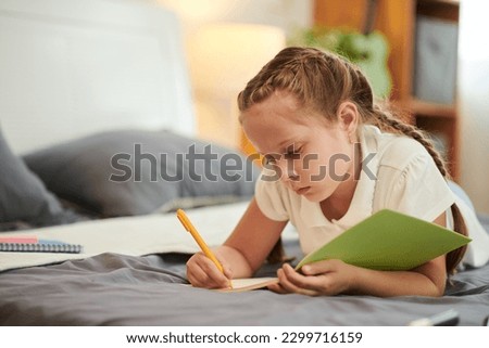 Pensive preteen girl lying on bed and writing in her diary