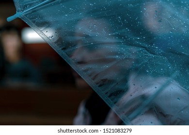 Pensive Pretty Girl Holding Transparent Umbrella While Strolling Outside On Rainy Autumn Day. Photo Looks Like Film Frame Or Movie Screenshot. Processed In Cold Colors