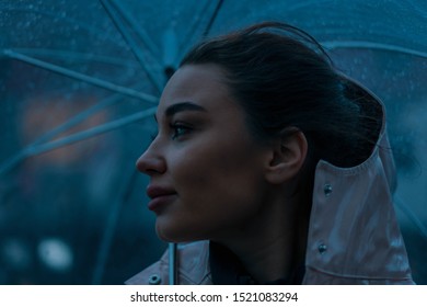 Pensive Pretty Girl Holding Transparent Umbrella While Strolling Outside On Rainy Autumn Day. Photo Looks Like Film Frame Or Movie Screenshot. Processed In Cold Colors