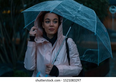 Pensive Pretty Girl Holding Transparent Umbrella While Strolling Outside On Rainy Autumn Day. Photo Looks Like Film Frame Or Movie Screenshot. Processed In Cold Colors