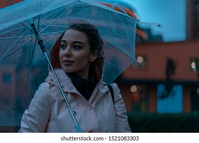 Pensive Pretty Girl Holding Transparent Umbrella While Strolling Outside On Rainy Autumn Day. Photo Looks Like Film Frame Or Movie Screenshot. Processed In Cold Colors