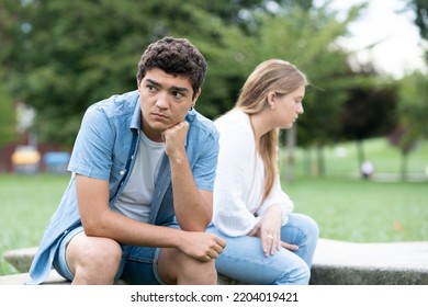 Pensive And Sad Hispanic Boy Thinking On Couple Relationship Sitting Back To Back With Girlfriend Outdoors In A Park