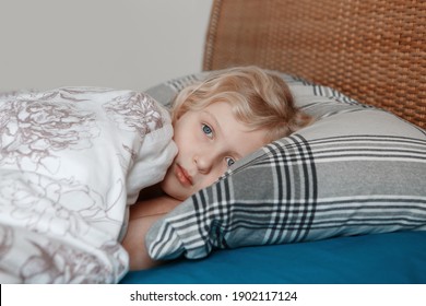 Pensive sad little Caucasian blonde child girl lying on pillow in bed at home. Child lying with open eyes thinking or dreaming. Candid authentic home life. Sweet dreams and bed vibes. 
