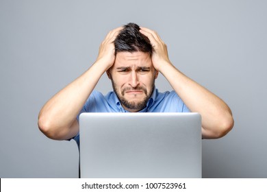 Pensive Sad Man Sitting At The Table With Laptop Over Gray Background