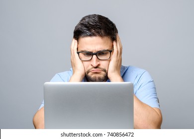 Pensive Sad Man Sitting At The Table With Laptop Over Gray Background