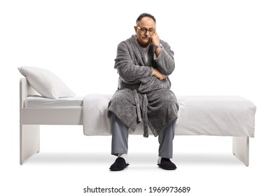 Pensive And Sad Mature Man In Pajamas And A Robe Sitting On A Bed Isolated On White Background