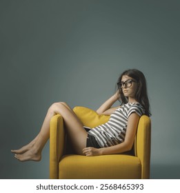 Pensive sad teen girl sitting sideways on a comfortable armchair and looking at camera, copy space