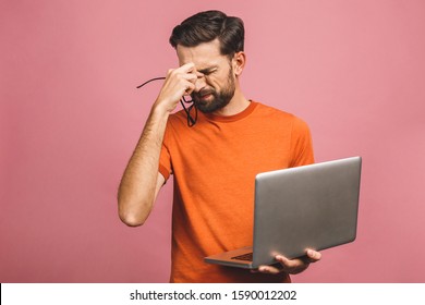 Pensive sad young man holding laptop isolated over pink background.
