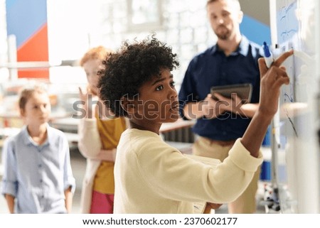 Pensive schoolkid solving equation on whiteboard in class