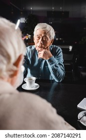 Pensive Senior Asian Man Looking At Blurred Friend During Meeting In Cafe