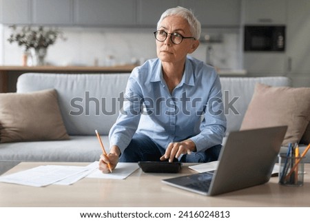 Pensive senior business woman sitting with laptop computer and taking notes on couch, writing report and conducting business online, sitting at modern home interior. Freelance Career