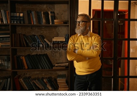 Pensive senior man standing with arms crossed on chest at home library