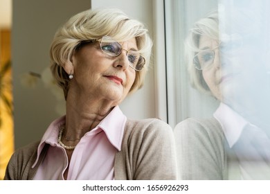 Pensive senior woman looking through the window while relaxing at home.  - Powered by Shutterstock