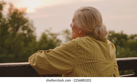 Pensive senior woman standing near fence alone, looking at sunset, life memories - Powered by Shutterstock