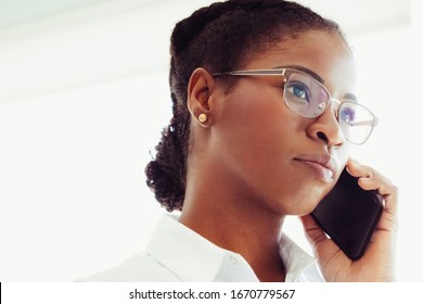 Pensive Serious Office Employee Talking On Mobile Phone. Closeup Of Young Black Business Woman Wearing Eyeglasses, Speaking On Cell. Telephone Concept