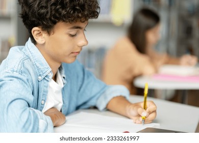 Pensive smart teenage boy taking notes, learning language, exam preparation, reading book  in modern classroom. Back to school, education concept - Powered by Shutterstock