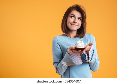 Pensive smiling young woman holding cupcake and thinnking