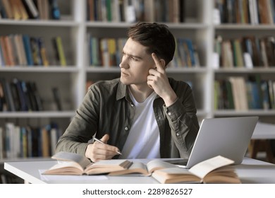 Pensive student guy stuck on difficult task for hours without progress, staring aside feels annoyed looks confused sit at desk with textbooks and laptop. Hard exercise, lack of skills or understanding - Shutterstock ID 2289826527