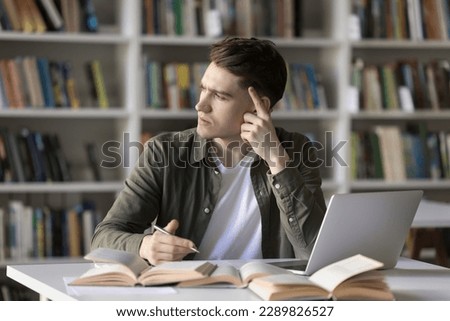 Pensive student guy stuck on difficult task for hours without progress, staring aside feels annoyed looks confused sit at desk with textbooks and laptop. Hard exercise, lack of skills or understanding