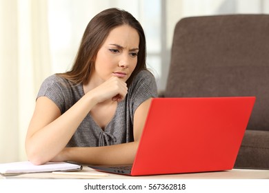 Pensive student studying on line with a red laptop sitting on the floor in the living room at home - Shutterstock ID 567362818