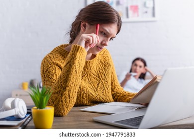 Pensive Teenager Reading Book While Studying Near Laptop At Home