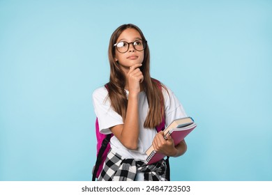 Pensive thoughtful caucasian schoolgirl teenager thinking about school education e-learning, holding copybooks and books isolated in blue background - Powered by Shutterstock