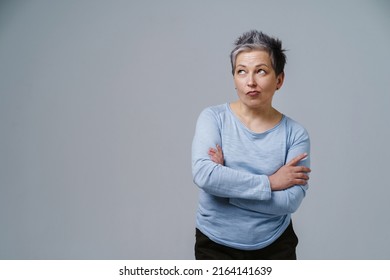 Pensive, thoughtful, doubt mature woman with grey hair in 50s posing with hands folded and copy space on left isolated on white background. Place for product placement. Aged beauty. Toned image.