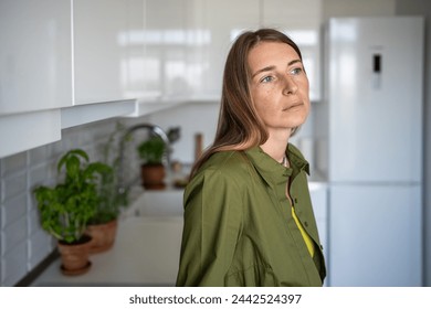 Pensive thoughtful woman with distressed mood stands in kitchen of home. Anxiety fear. Tired frustrated blonde woman feel bad, looking sadly away. Mid-life crisis, despair, sadness, negative emotions.