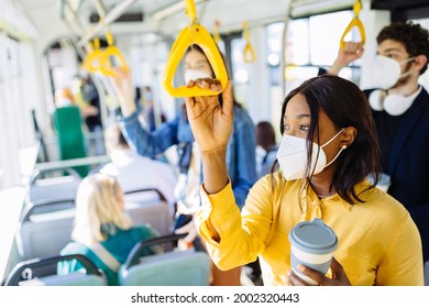 Pensive Tired Black Woman Commuting Work By Bus And Wearing Protective Face Mask Due To Coronavirus Pandemic. Thoughtful African American Girl Holding Handles In Bus Or Subway Train.