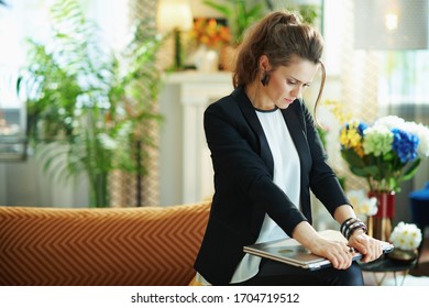 Pensive Trendy Woman In White Blouse And Black Jacket With Closed Laptop Sitting On Couch In The Modern House In Sunny Day.