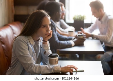 Pensive upset young rejected girl waiting for boyfriend to come on first date in cafe, frustrated social outcast or loner sitting alone at coffeeshop table with phone offended excluded by friends
